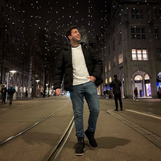 Tobias steht auf der Straße und schaut gen Himmel. Über ihn erleuchten Straßengirlanden, denn er ist zur Adventszeit in Zürich gewesen.