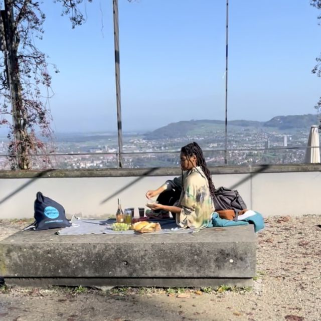 Eine Freundin von Tobias sitzt auf einem Handtuch und picknickt. Hinter ihr siht man eine weitreichende Aussicht über die Stadt Bern.