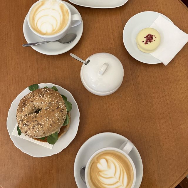 Tisch von oben mit zwei Tassen Kaffee, einem Bagel, und einem rundem Törtchen.