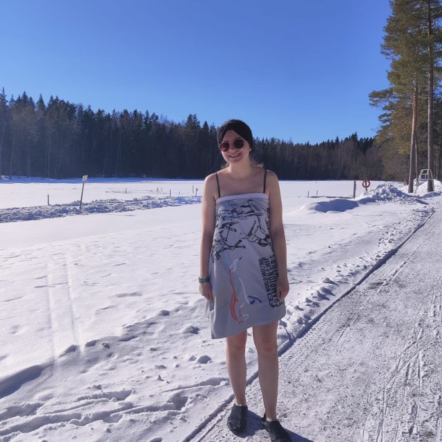 Junge Frau steht nur mit einem Handtuch bekleidet im Schnee, die Sonne scheint