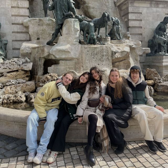 meine drei Schwestern und zwei Freunde sitzen auf dem rand von einem Brunnen in Budapest und umarmen sich.
