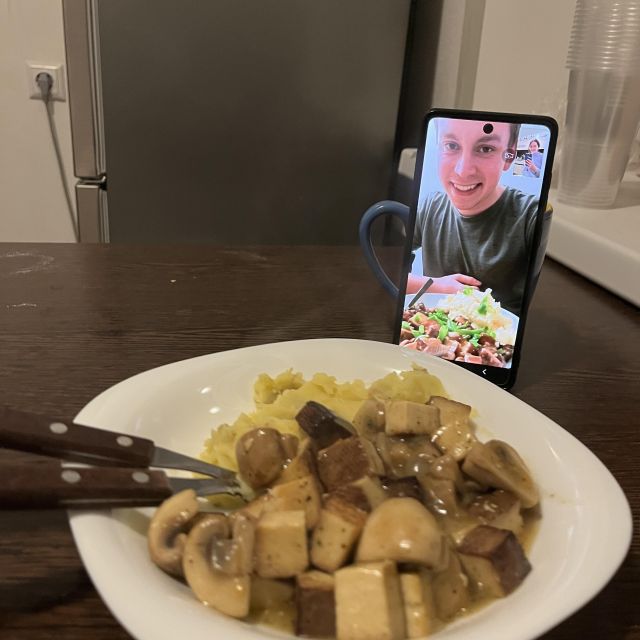 Voller Teller mit gekochtem Essen, daneben ist ein Handy angelehnt, auf dem ein Videoanruf läuft
