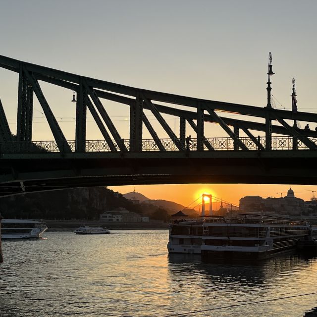 Das Donauufer bei Sonnenuntergang. Im Vordergrund ist ein Teil der Freiheitsbrücke zu sehen