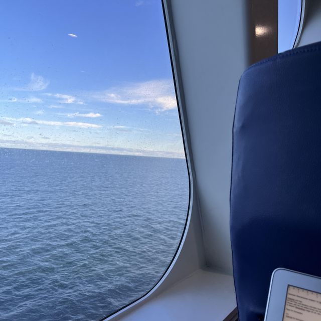Das Foto ist aus dem Fenster einer Fähre aus aufgenommen, man sieht das Meer und blauen Himmel.