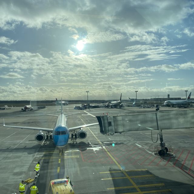 Blick aus dem Fenster am Flughafen auf ein Flugzeug, das zum Boarding bereitsteht. Im Hintergrund Sonne und Wolken am Himmel.